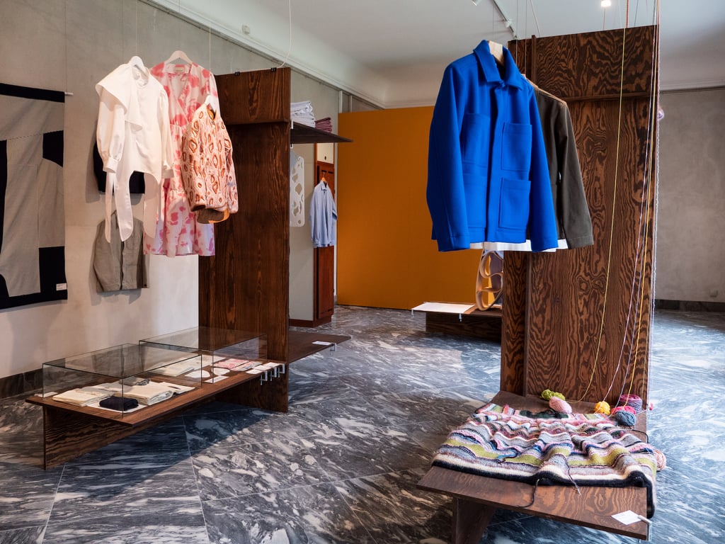 A room in a museum, where three items of clothings are hanging in an exhibition layout