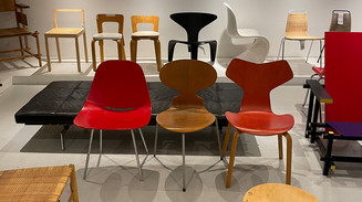 En kurateret udstilling af danske og internationale designklassikere i en stolesamling. Stole i træ, formspændt finér, plast og flettede materialer er arrangeret i rækker og viser forskellige former, farver og perioder i moderne møbeldesign.
