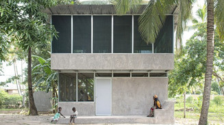Modern two-story house surrounded by palms and trees, with children and an adult outside.