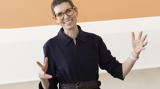 : Sofie Beier smiler og gestikulerer med begge hænder foran en orange og hvid baggrund.