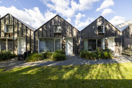 Small timber-clad houses with private entrances and green spaces in front.