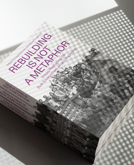 Stack of books titled ‘Rebuilding Is Not a Metaphor’ lying in patterned light and shadow.