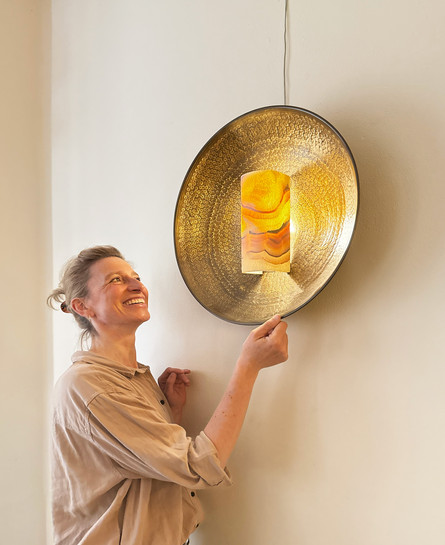 erson undersøger vægmonteret lampe med gylden skærm.