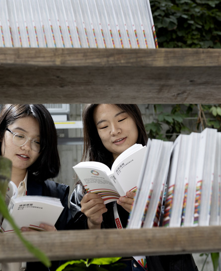 Visitors browsing and reading books on a display shelf in a green indoor setting.