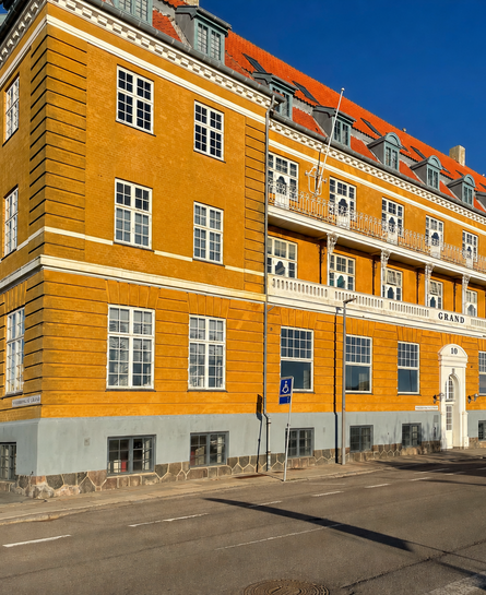 Historisk gul bygning med rødt tegltag og altaner langs en bred gade.