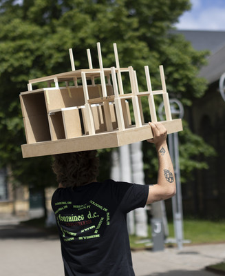 Person bærer en arkitekturmodel gennem et gårdrum mellem historiske bygninger.