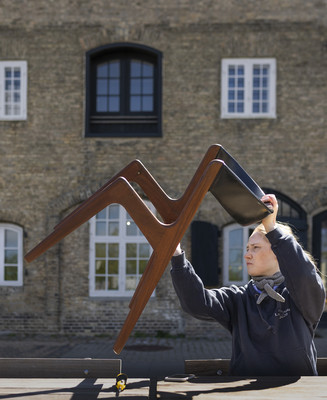 Person løfter en stol udendørs foran en historisk murstensbygning.