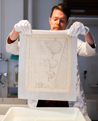 Person med hvide handsker holder et historisk arkitektonisk tryk til konservering.