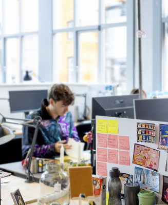 Studerende arbejder ved skriveborde i et lyst studiemiljø med inspirationsvægge.