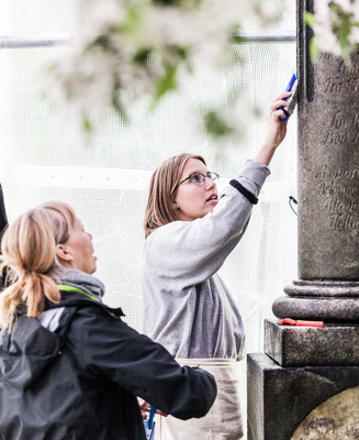 To personer rengør en indgraveret stenmonument med bløde børster.