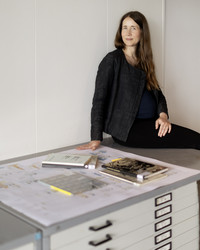 Color photograph of Christine Bjerke sitting on a archive furniture with archival materials next to her. 