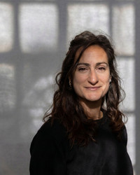 Picture of Roberta with shoulder-length brown hair and fair skin, wearing a light-colored t-shirt, looking directly at the camera with a neutral expression against a soft, light background.