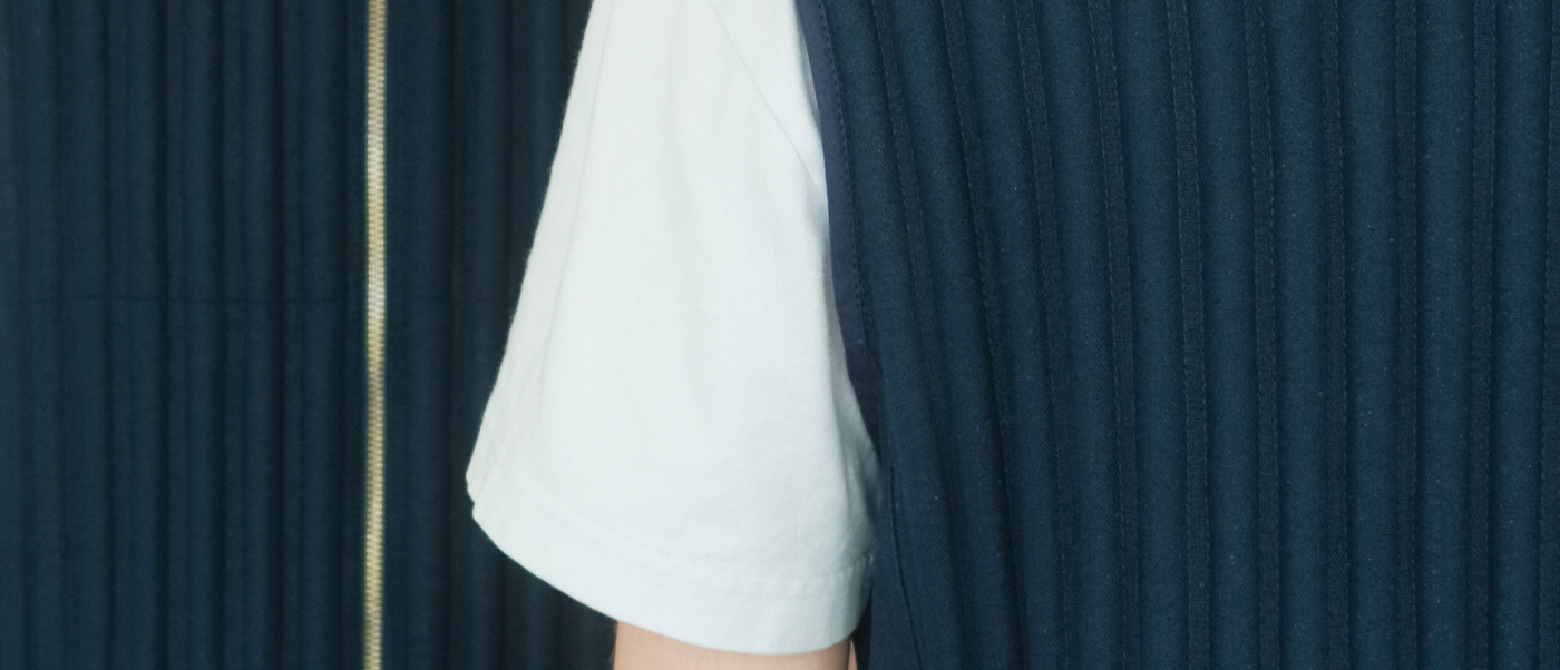 Close-up of two people wearing dark pleated vests, showing front and back details.