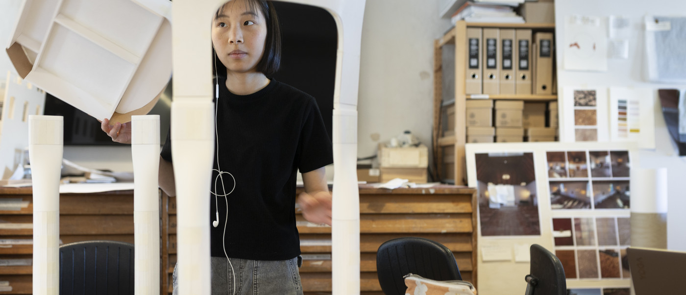 Person assembling a white chair prototype at a worktable.