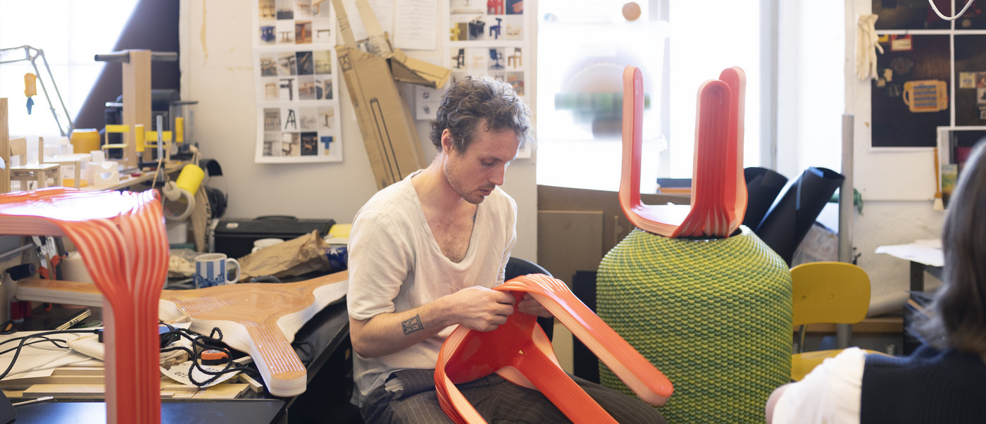 Person shaping bright red chair parts in a workshop.