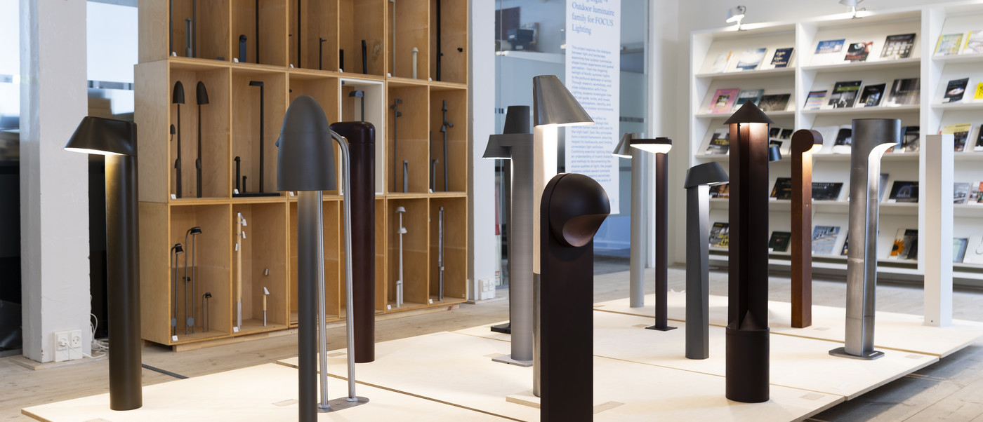 Display of outdoor light fixtures on platforms with shelving and books in the background