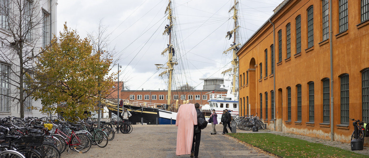 People walking near bicycles and a tall ship.