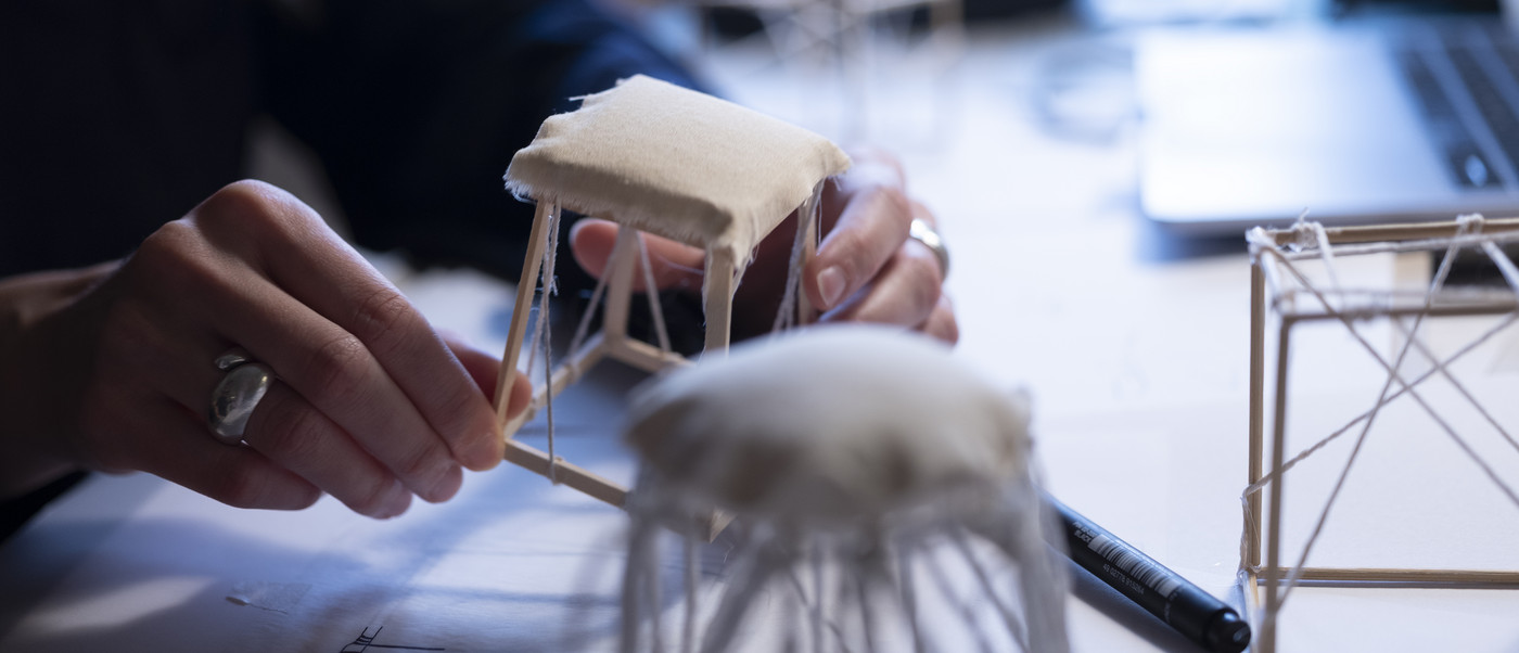 Hands working on a small chair model made of wood and textile.