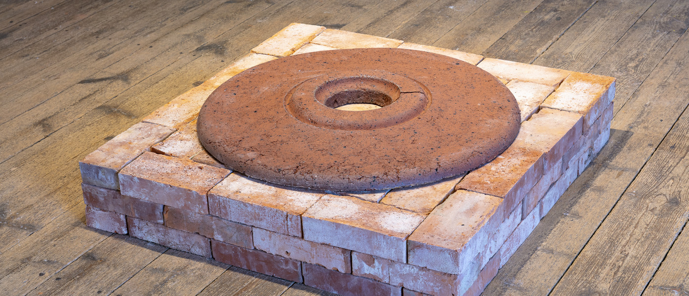 Square brick structure with circular rusted disk on top.