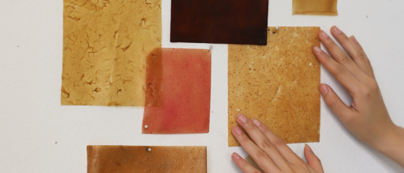 Material samples in warm tones pinned to a wall, with hands touching them.