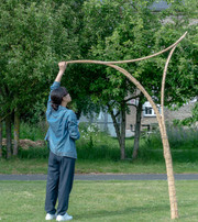 Person adjusting a curved bamboo structure on a lawn.