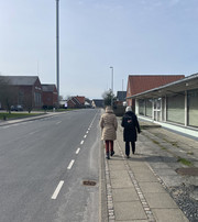 To personer går langs fortovet i en mindre by med lave bygninger