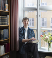 James sitting by the window in a library, with a book in his hands.