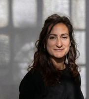 Picture of Roberta with shoulder-length brown hair and fair skin, wearing a light-colored t-shirt, looking directly at the camera with a neutral expression against a soft, light background.