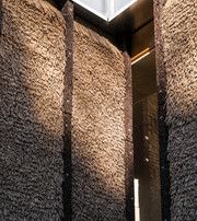 Façade detail with tightly packed bundles of thatching straw secured between dark vertical panels beneath metal cladding.