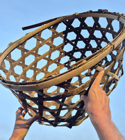 Two hands holding a basket woven from wooden strips against a blue sky.
