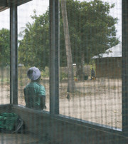 Person wearing a green jumper and a white hat stands outside a building with large mesh-covered windows.