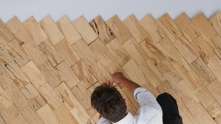 Person arranging small wooden pieces in a diagonal pattern on a wall.
