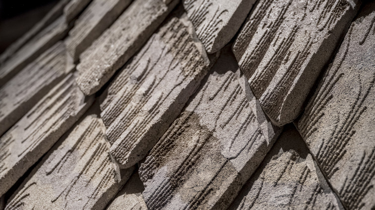 Close-up of overlapping pale panels with rough surfaces and engraved, wood-like patterns.