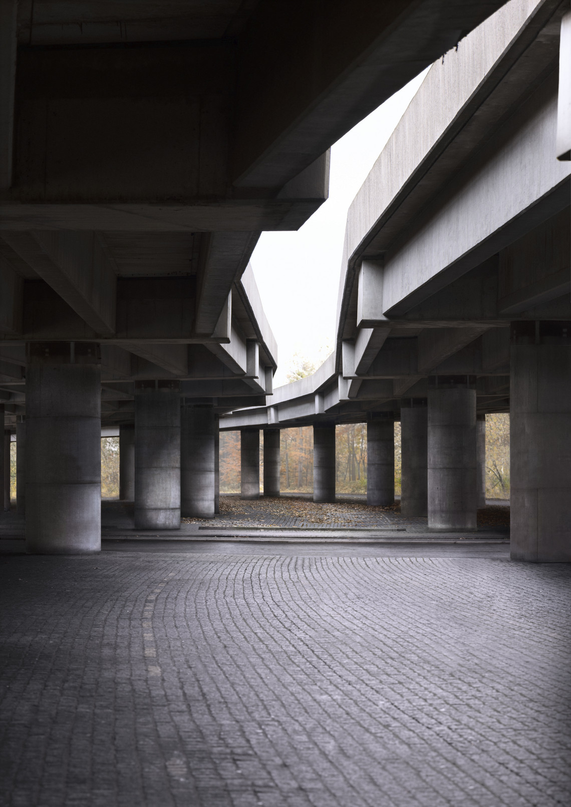 Udsigt under vejbro med betonpiller og brostensbelægning.