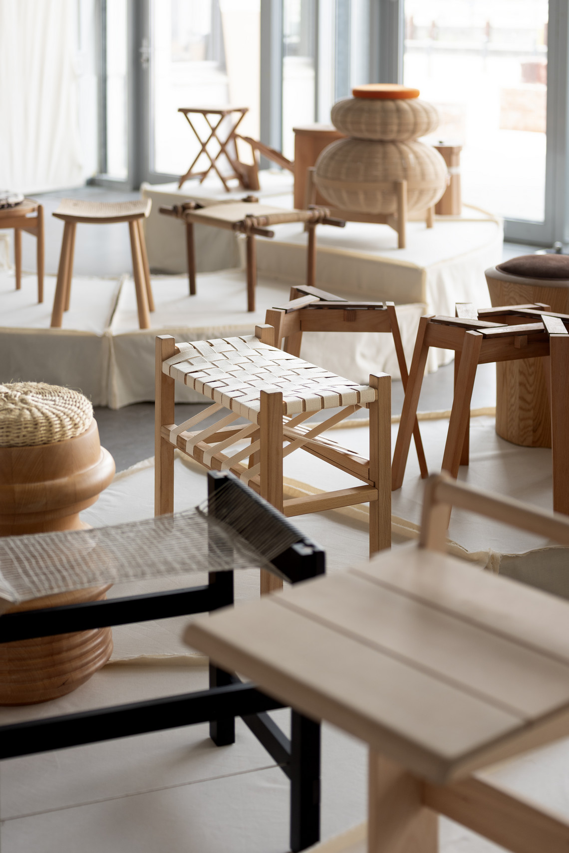 Exhibition of wooden stools and seating designs on plinths.