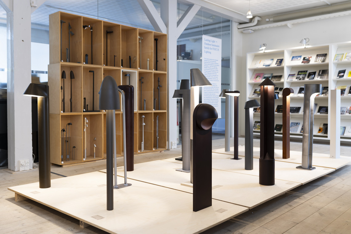 Display of outdoor light fixtures on platforms with shelving and books in the background