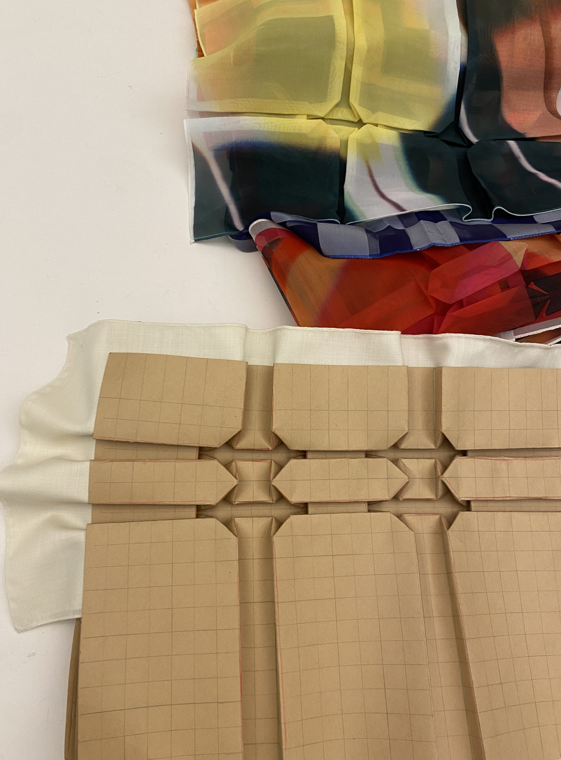 Layered colorful fabric samples above folded paper prototypes on a work surface.