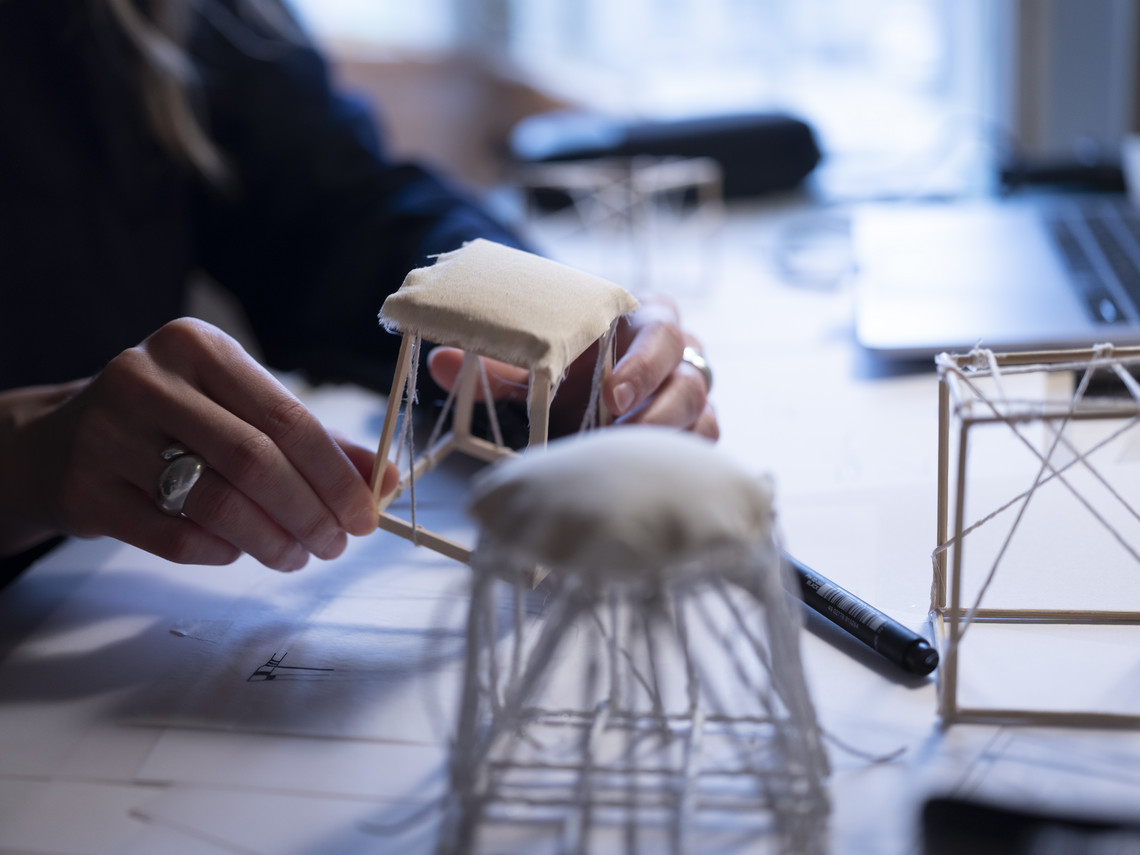 Hands working on a small chair model made of wood and textile.