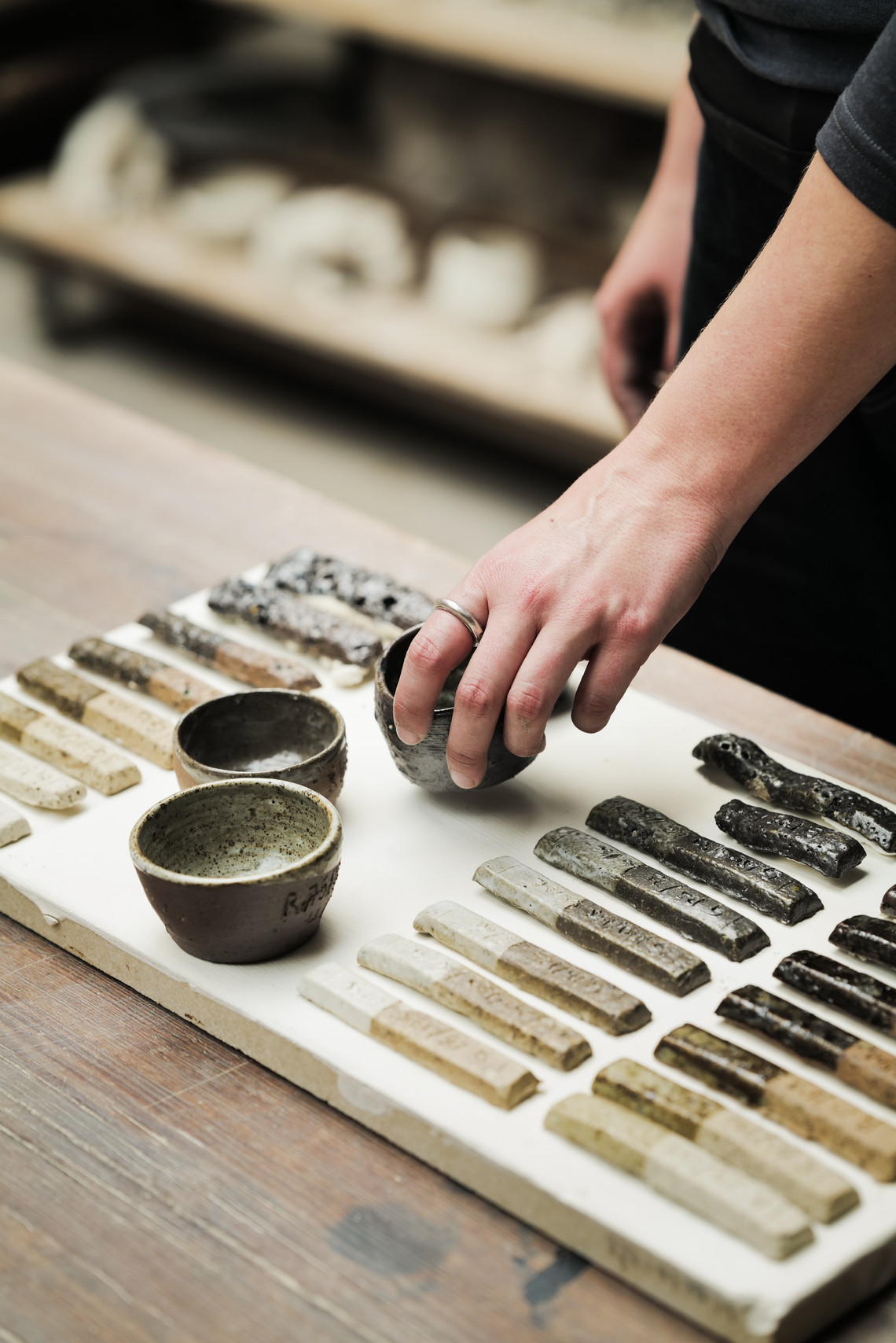 Hand placing ceramic samples and small bowls on a board.