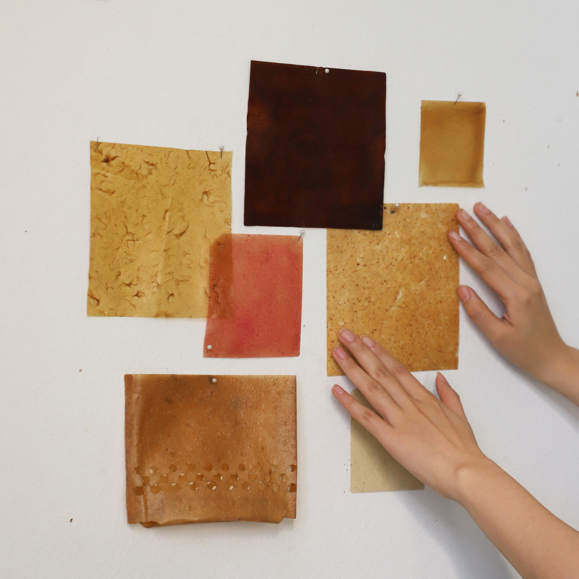 Material samples in warm tones pinned to a wall, with hands touching them.