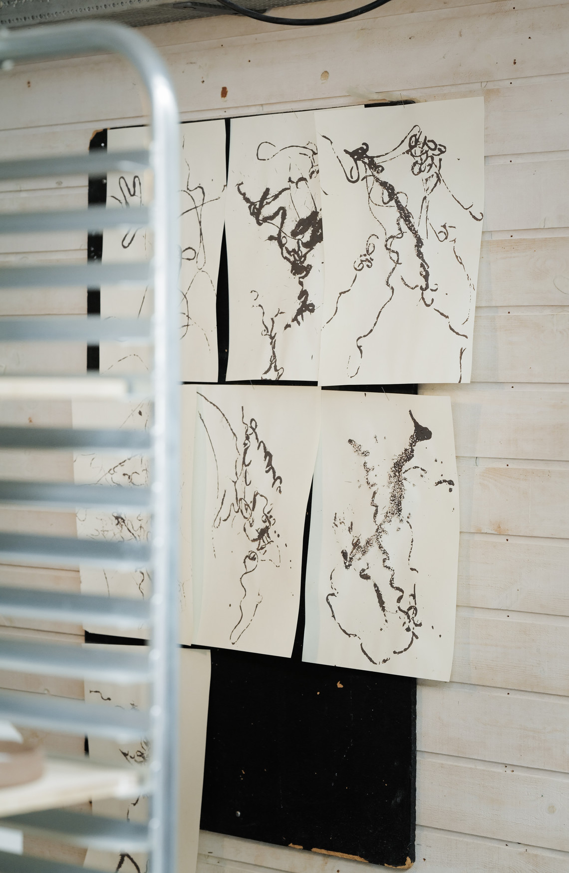 Abstract ink drawings pinned to a wall in a studio.
