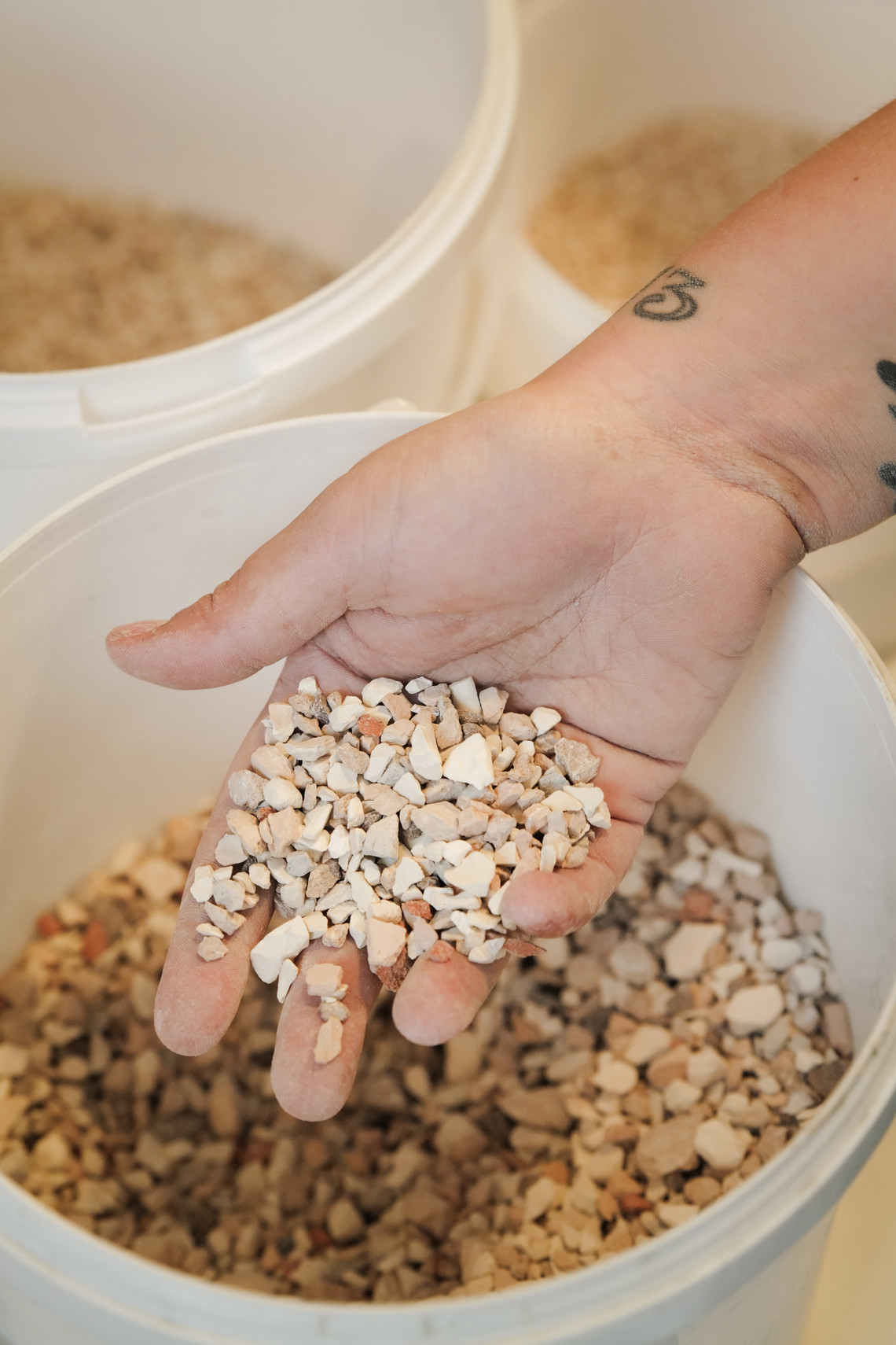 Hand holding crushed ceramic fragments over a bucket.