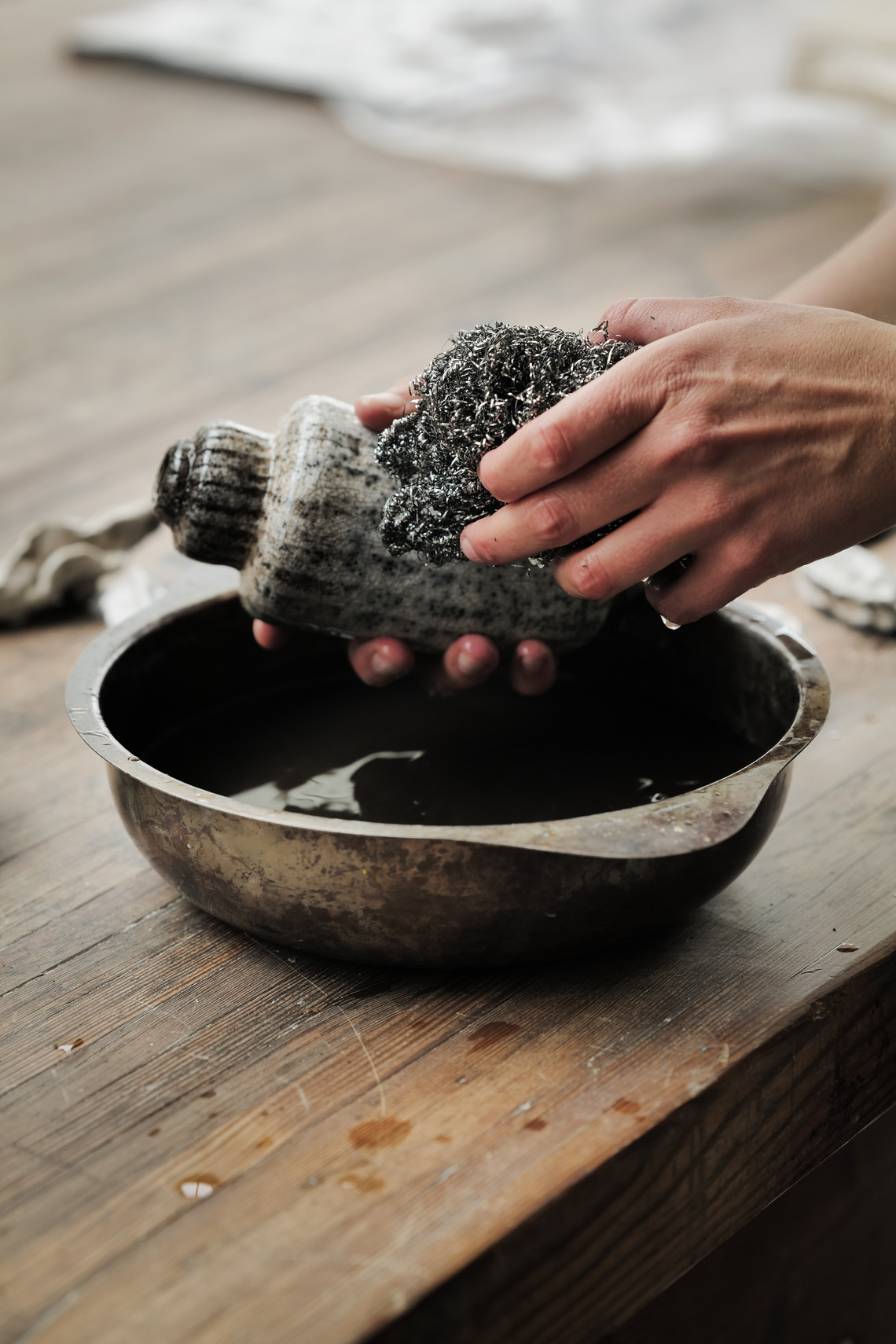 Hands cleaning a ceramic vessel over a bowl of water.