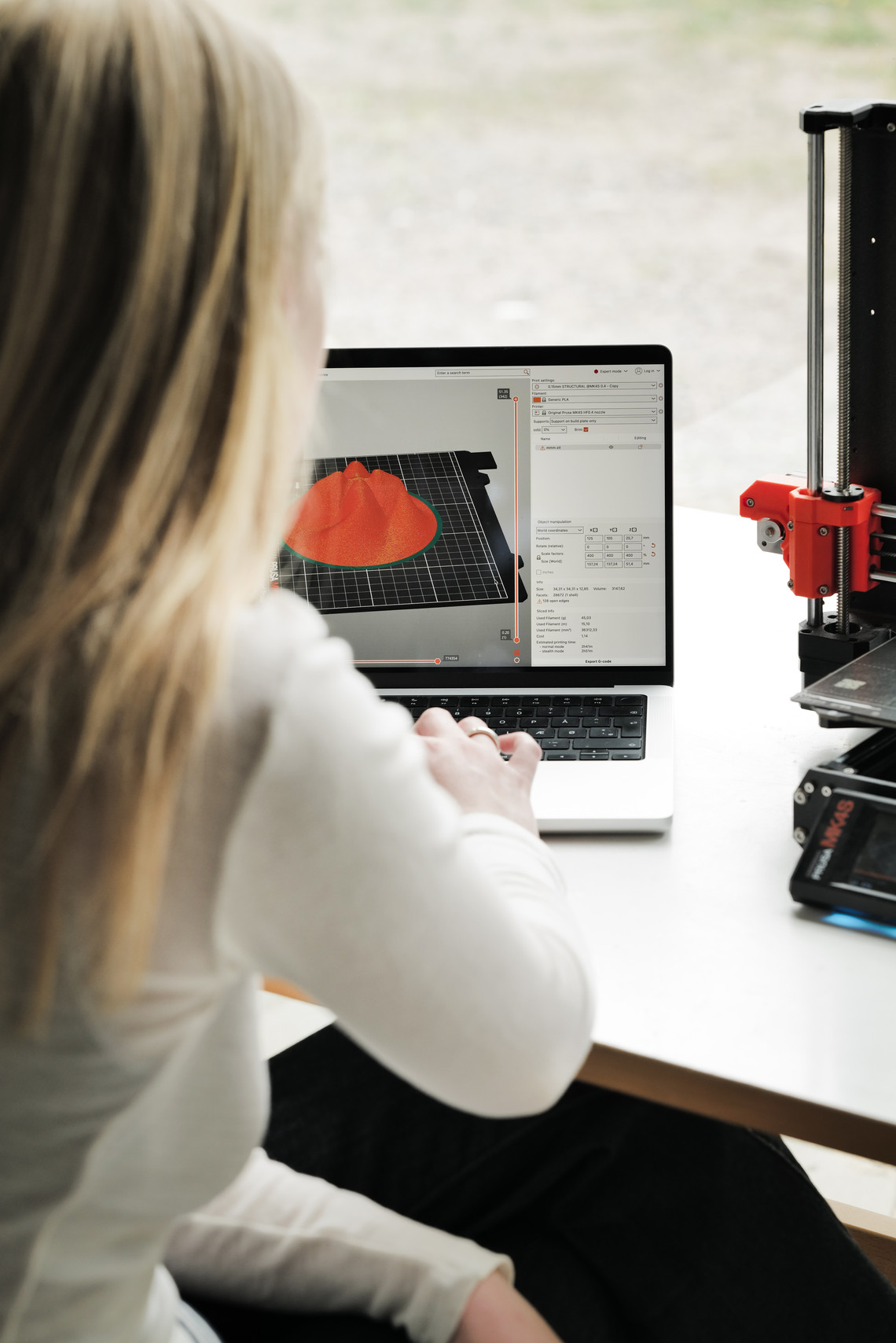 Person using a laptop with a 3D model next to a 3D printer.