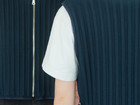 Close-up of two people wearing dark pleated vests, showing front and back details.