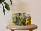 Small textured lump in yellow and green on a wooden stool.