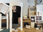 Person assembling a white chair prototype at a worktable.