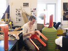 Person shaping bright red chair parts in a workshop.
