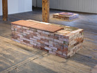 Brick installation in gallery space on wooden floor.