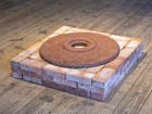 Square brick structure with circular rusted disk on top.